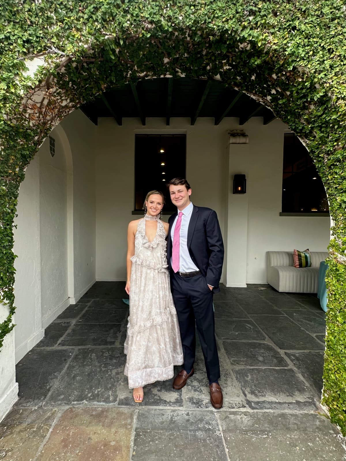 Allie and Chris dressed for a wedding beneath an ivy-covered arch